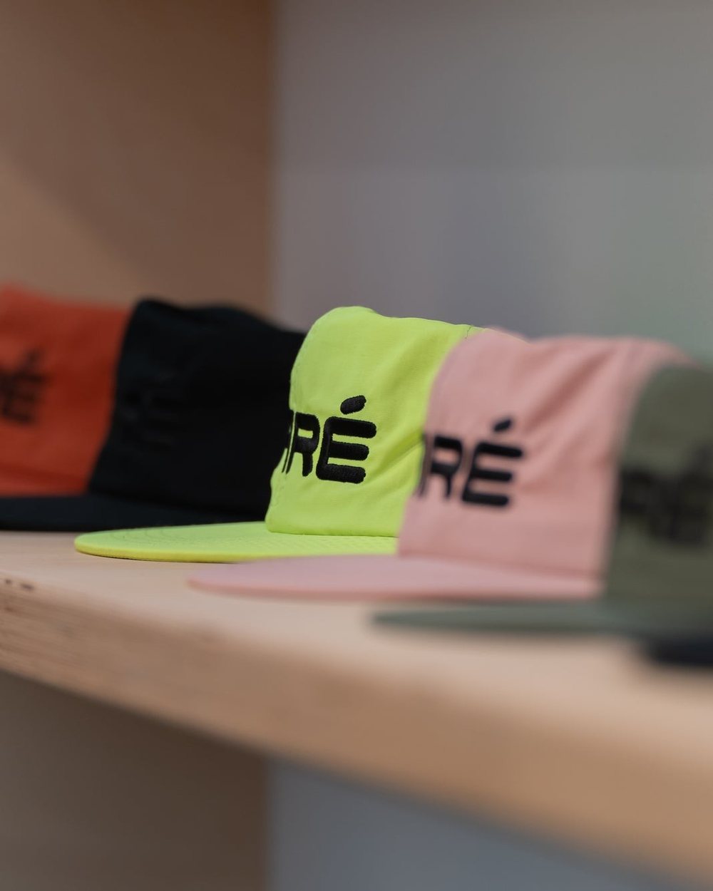 A row of Paré nylon hats in orange, black, neon yellow and pink on a wooden shelf