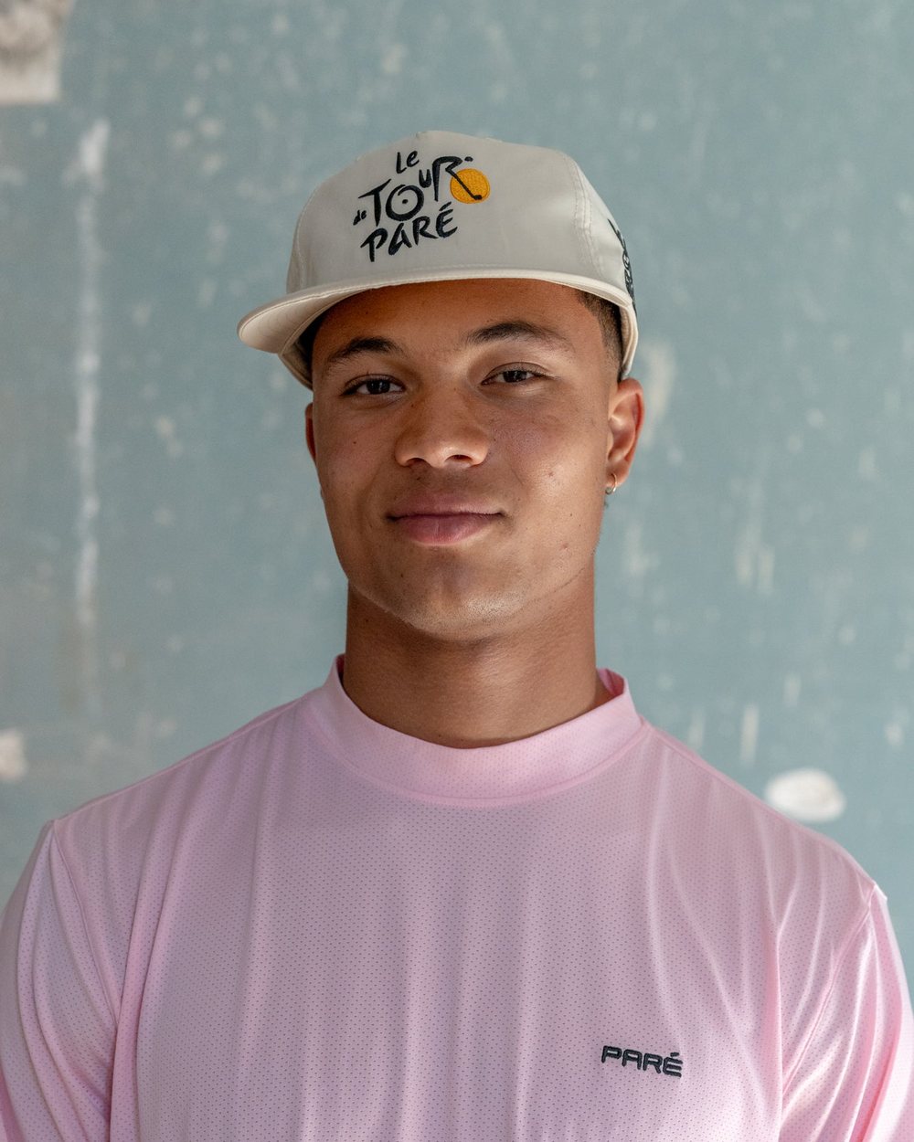 A man in a pink long sleeve and the cream Paris Golf Gallery x Paré cap smiling at the camera