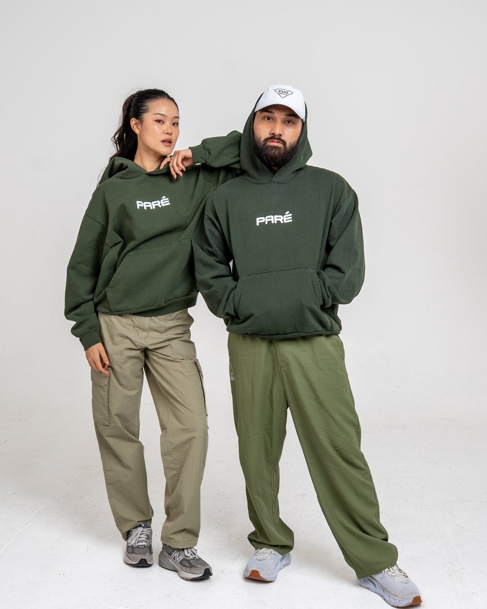 Two people in forest green Gulay hoodies and green trousers standing together