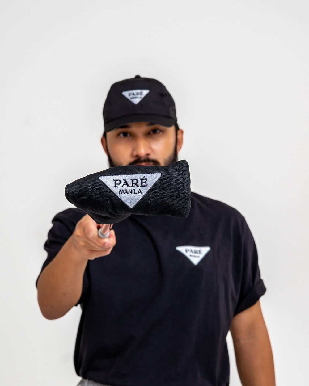 A man in a black Manila tee holding the Bluetross putter cover up to the camera
