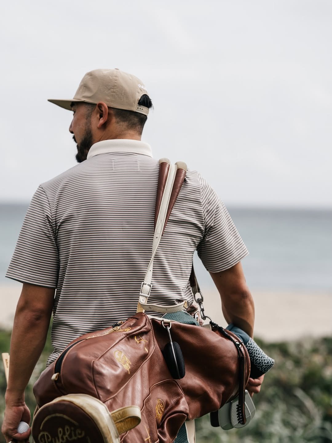 A golfer on a beach carrying a leather Public Drip carry bag