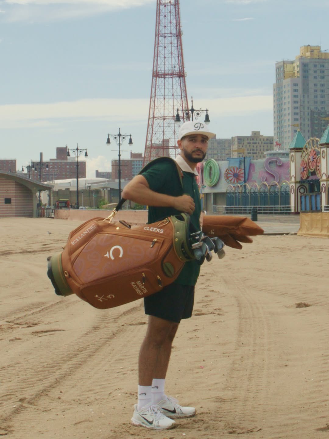 A golfer on the sand at Coney Island carrying a leather golf bag