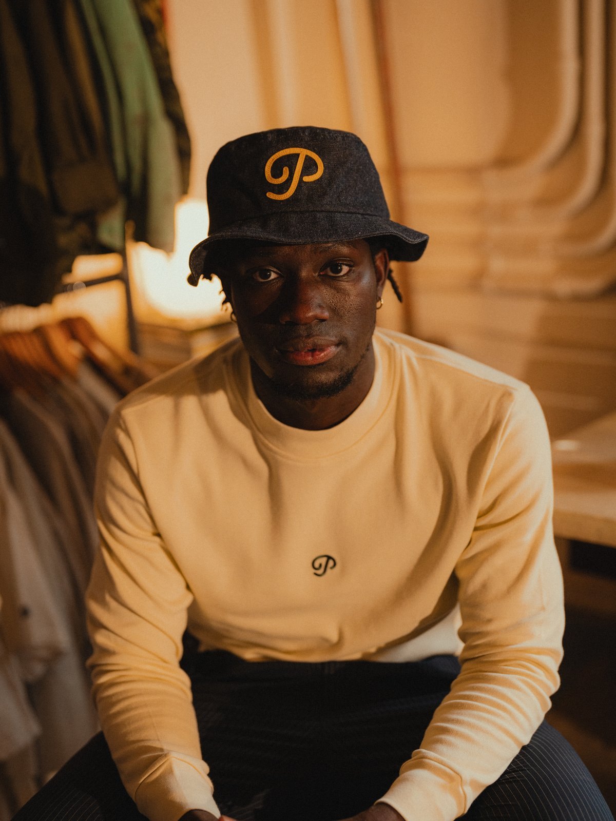 A man in a cream long-sleeve mock and denim P script snapback