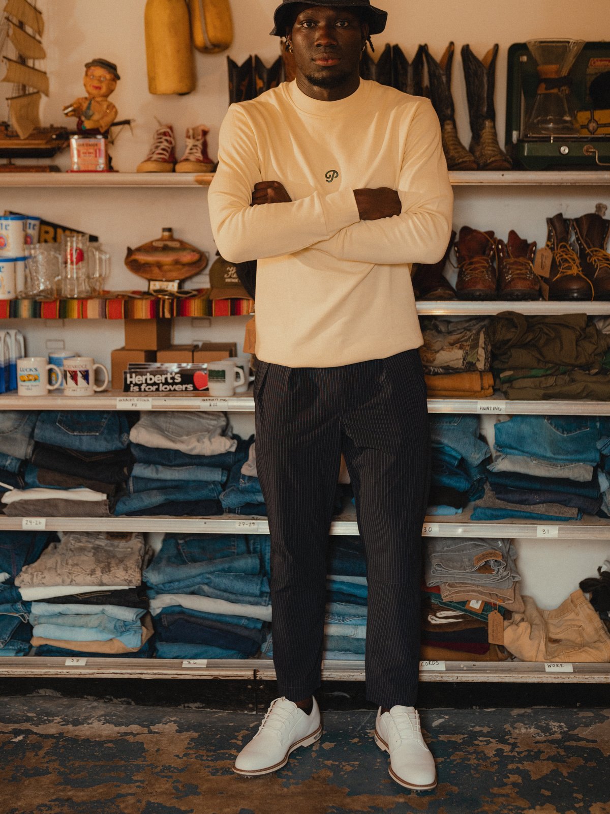 A man in a cream knit standing in front of shelves of vintage denim and boots