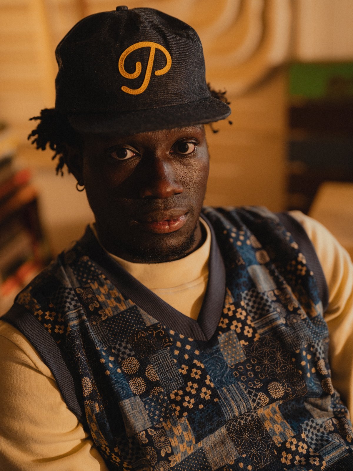 Close portrait in the patchwork swing vest and a denim P script snapback