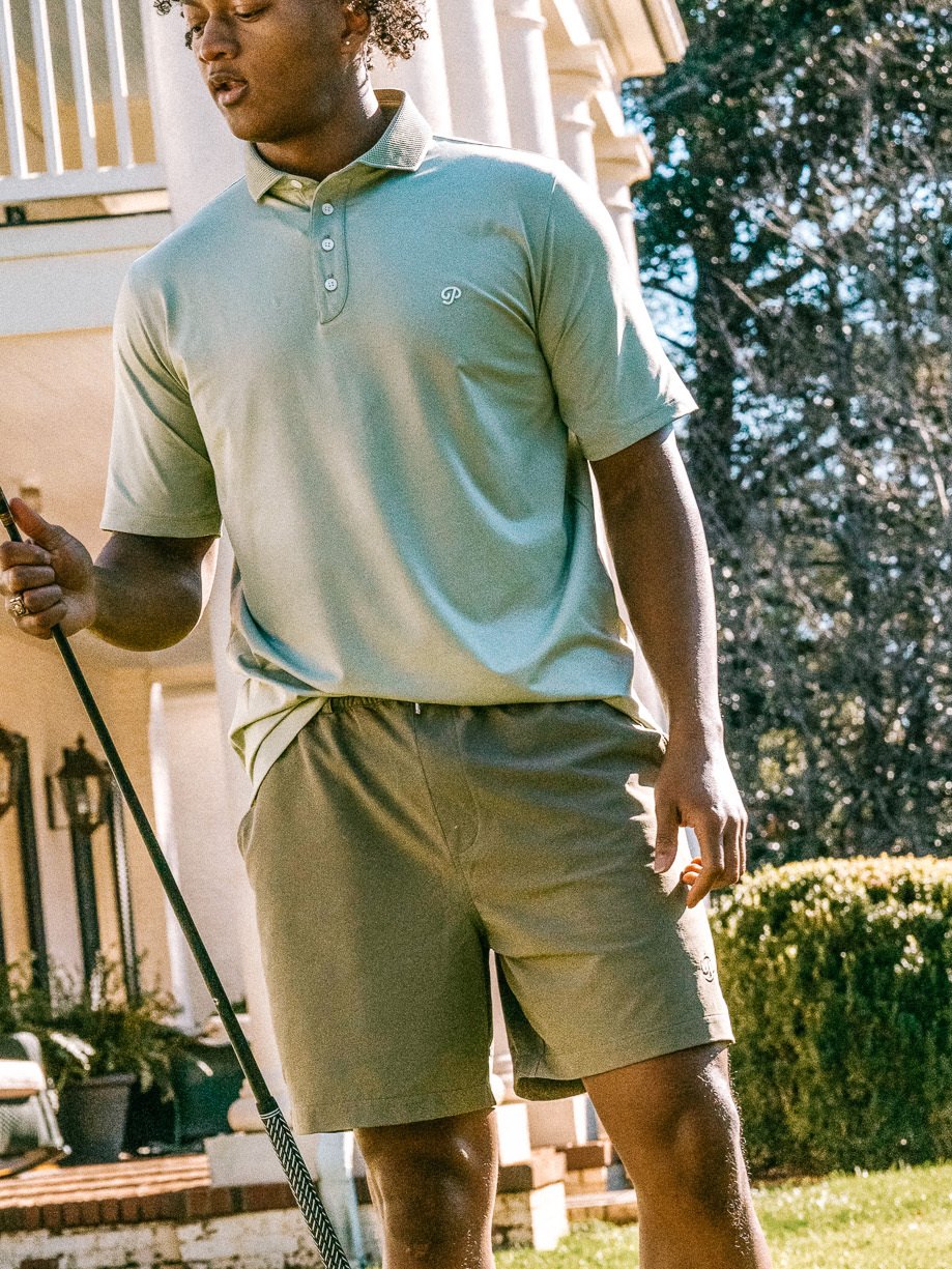 A golfer in a mint polo and olive shorts on a lawn