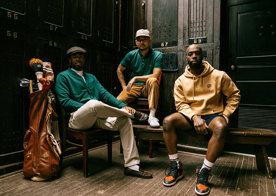 Three golfers in Public Drip sitting on a bench by a stone building