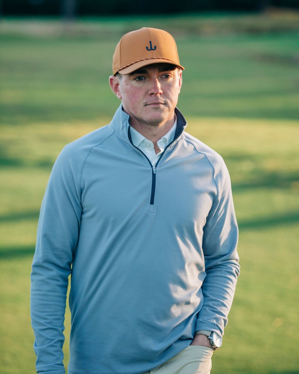 A golfer in a light-blue Juniper & James performance quarter-zip on a course at golden hour