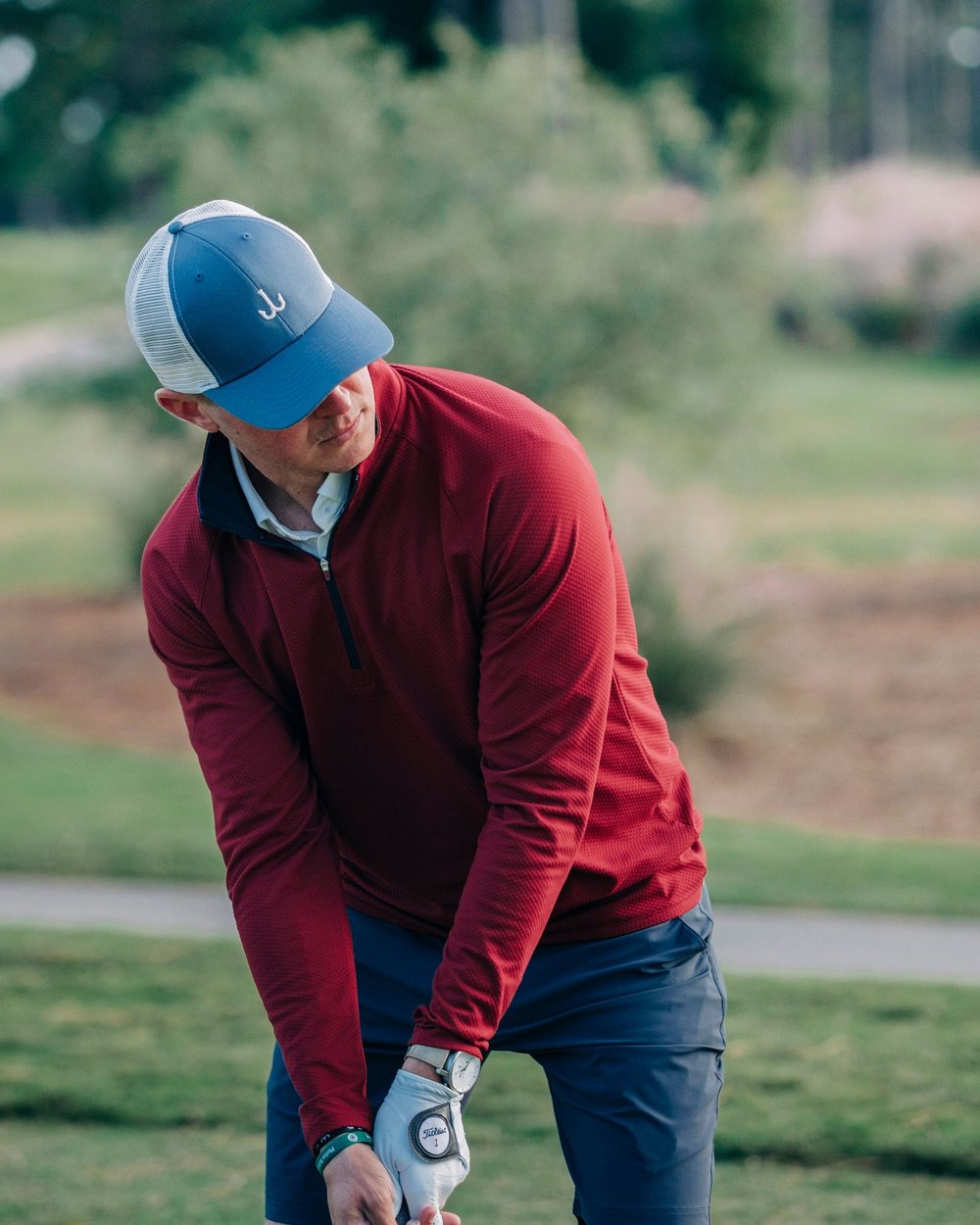 A golfer in a maroon Juniper & James quarter-zip addressing the ball