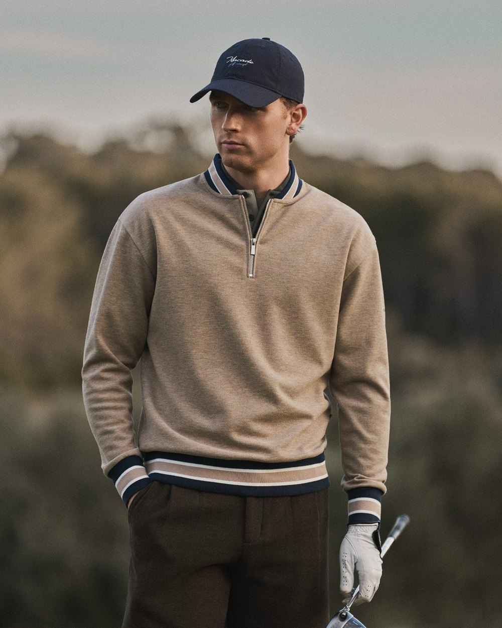 A golfer in a heather-tan Macade quarter-zip with varsity trim, iron in hand