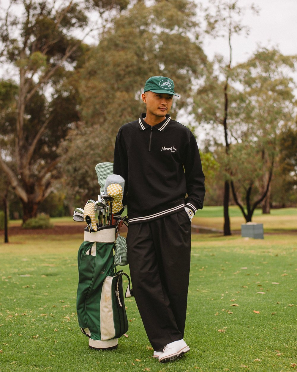 A golfer in a black Mount Tee tipped-collar quarter-zip on a parkland course beside a green bag