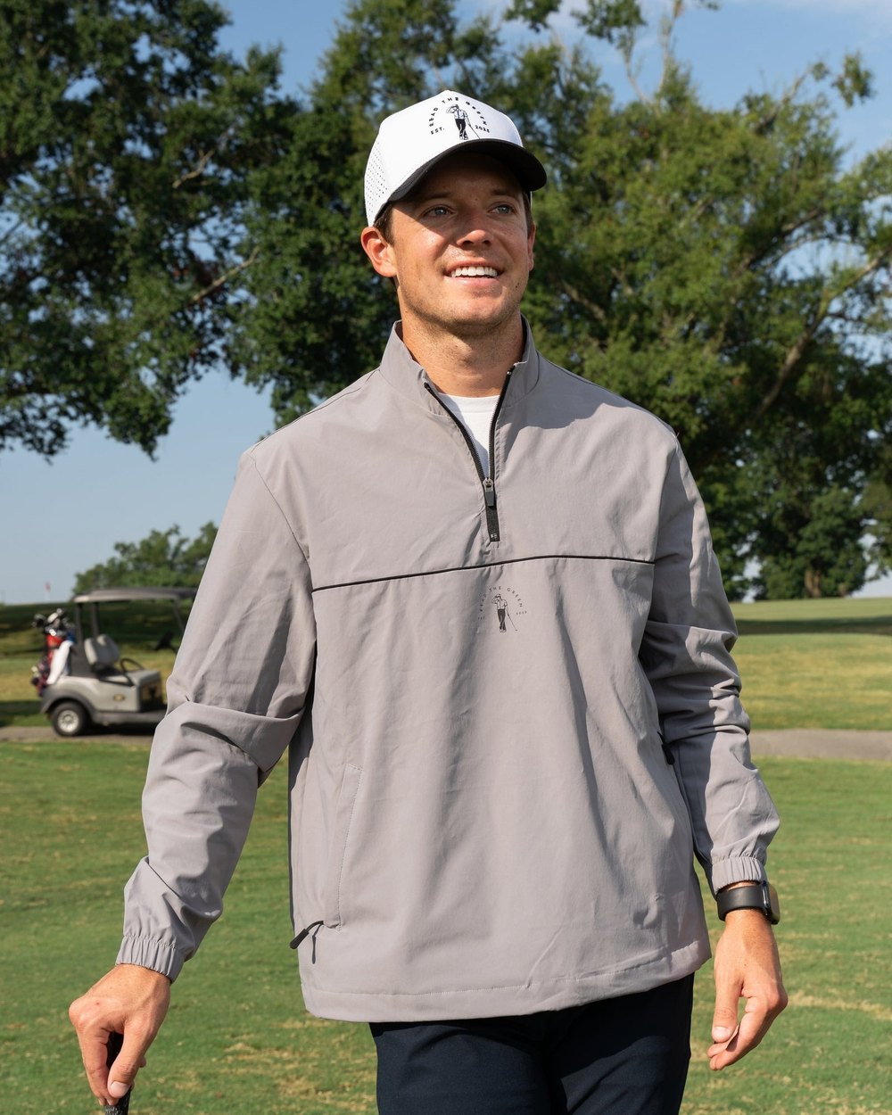 A golfer in a grey Read the Green half-zip windshirt walking on a course