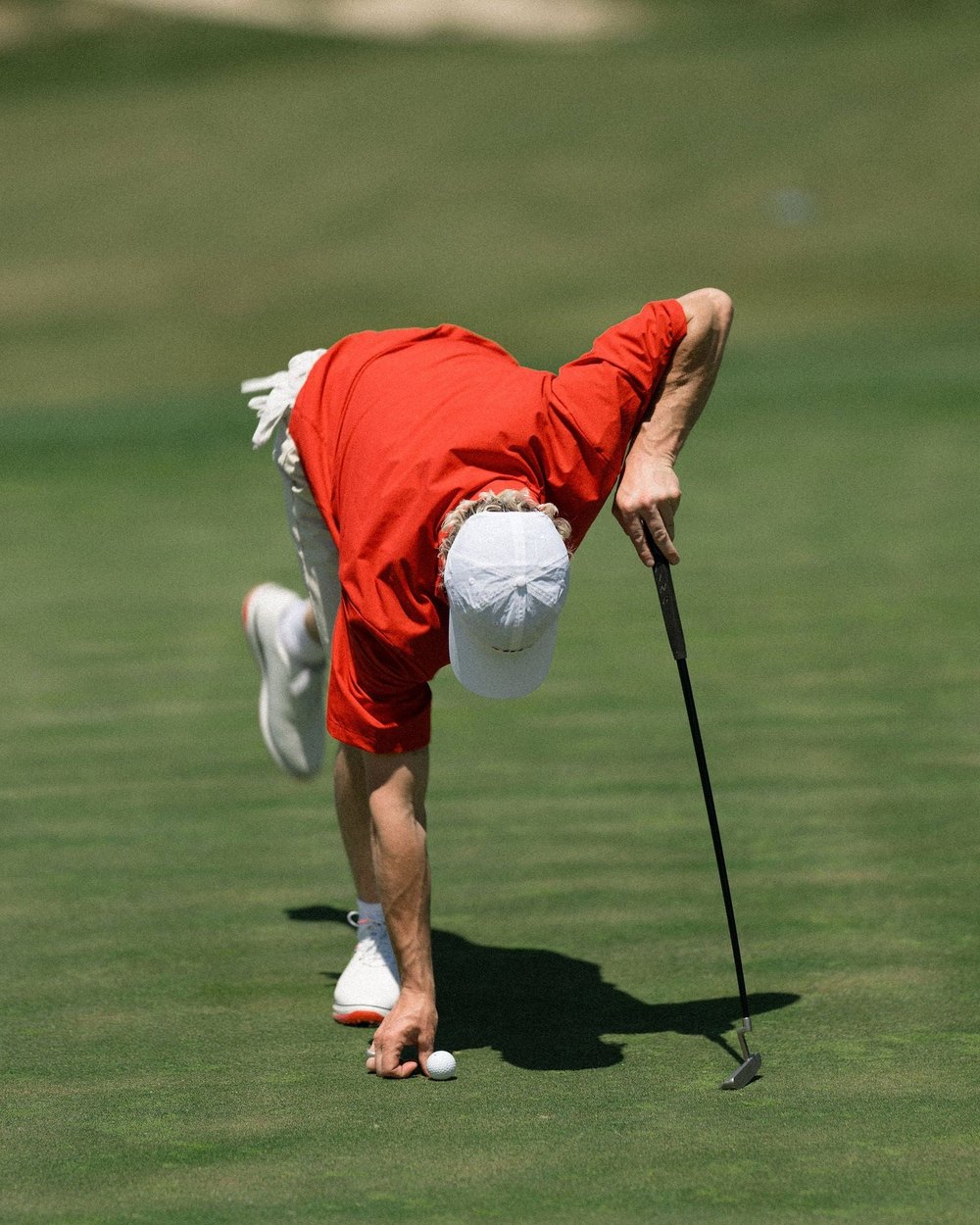 A golfer in a red Sugarloaf half-zip windshirt marking his ball on a green