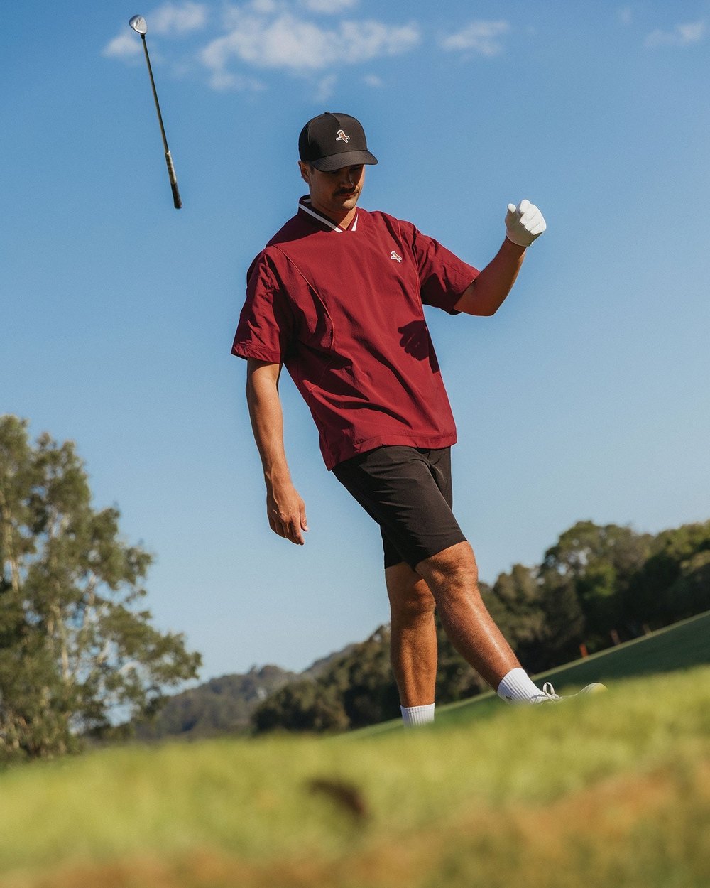 A golfer in a maroon Walker short-sleeve windshirt tossing a club after a shot