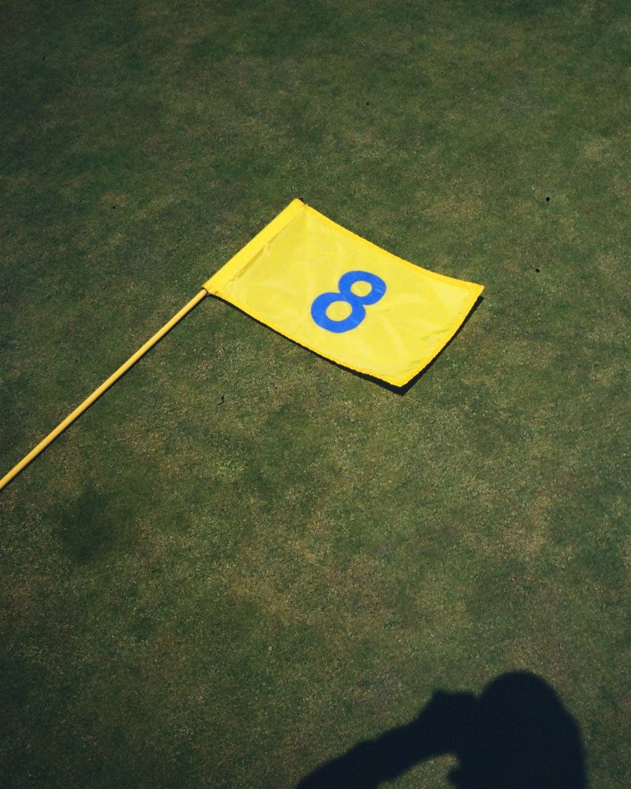 A yellow number eight flag lying on a green with a golfer's shadow