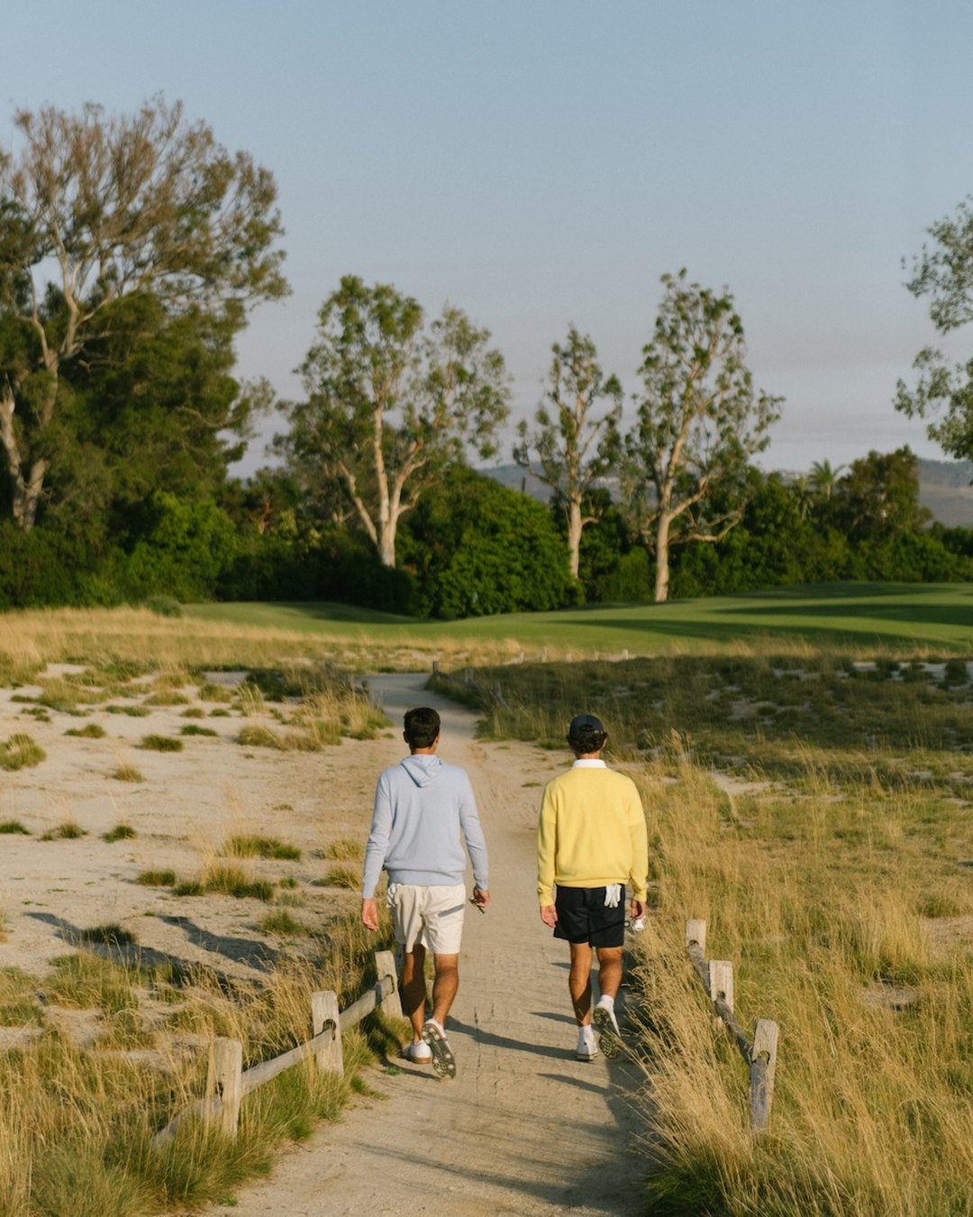 Two golfers walking a sandy path between the fairways