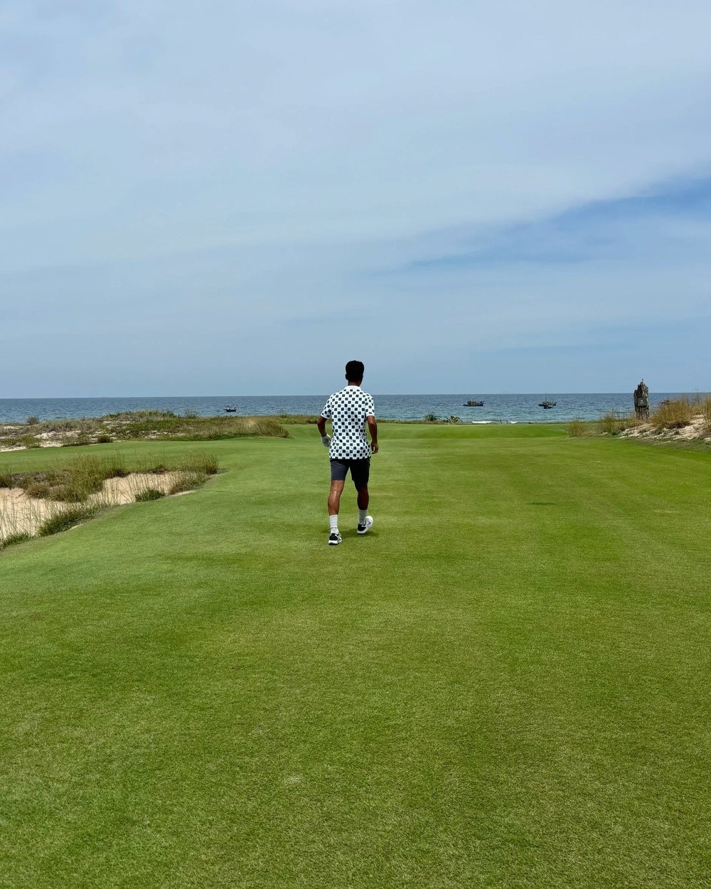 A golfer walking down a wide fairway toward the sea