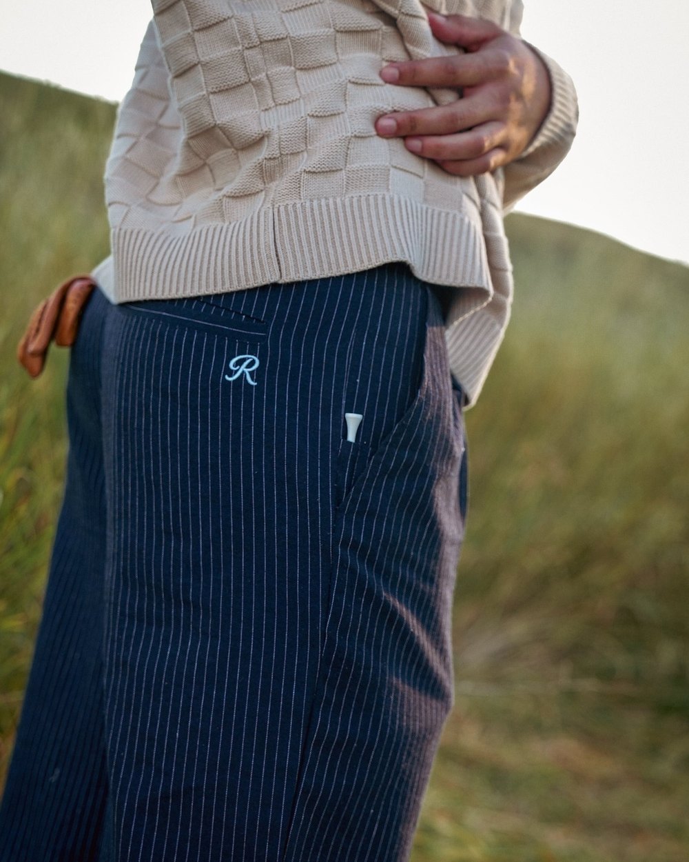 Close-up of navy pinstripe Rowena linen trousers on a grassy hillside