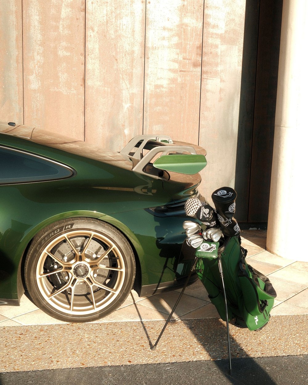 A DRVN golf bag with snail headcovers leaning on the wheel of a green sports car