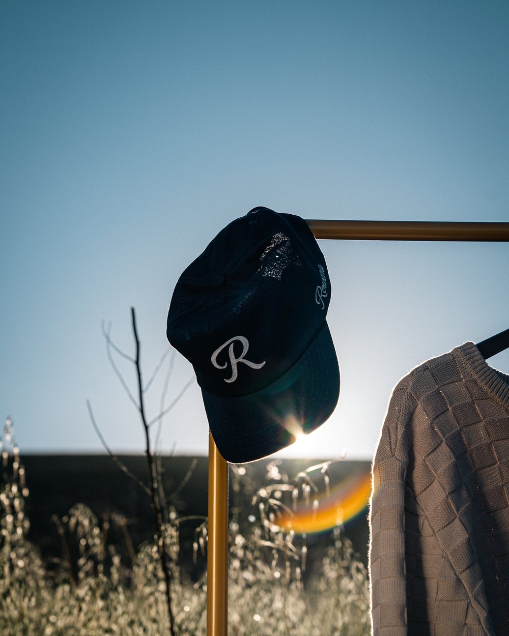 A navy Rowena R hat hanging on a rail at sunset