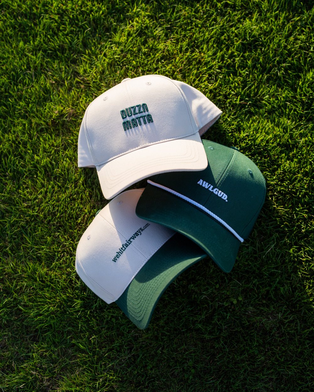 Three We Hit Fairways caps in white and green lying in the grass