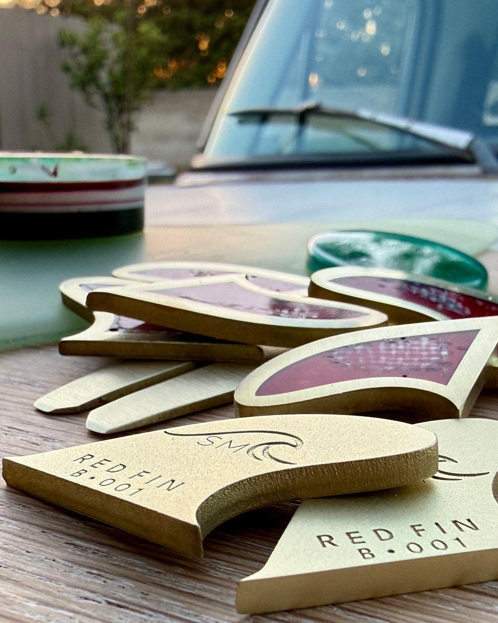 Brass Red Fin markers shaped like surfboard fins scattered on a wooden table