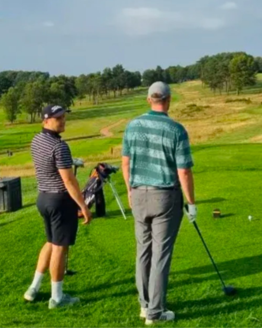 Two golfers waiting on a tee box on a green, rolling course