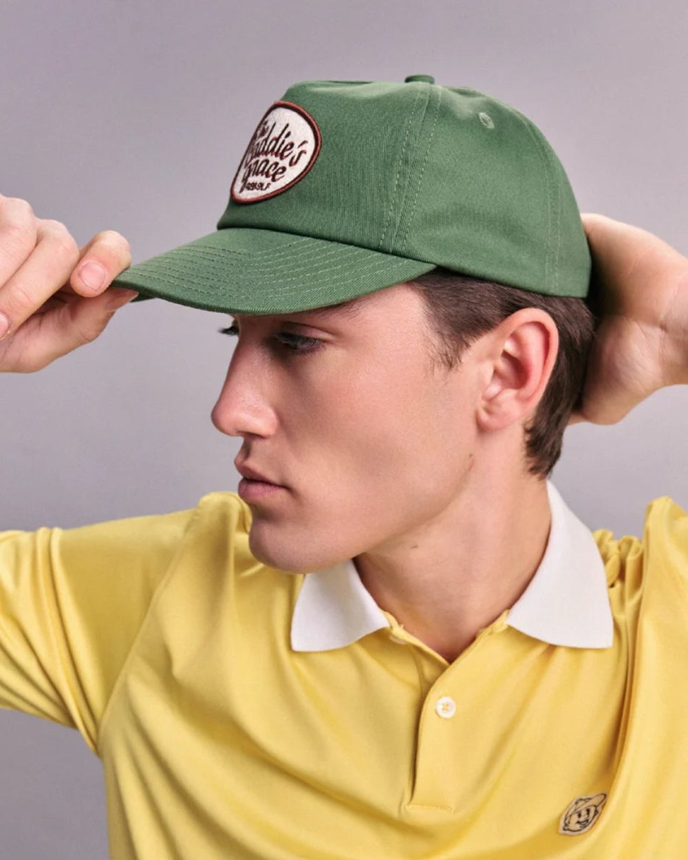 A model in a yellow Rebolf polo adjusting a green Caddie’s Grace cap