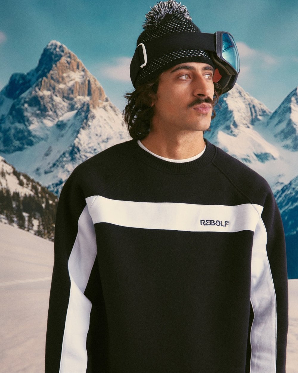 A model in a black and white Rebolf sweater in front of a snowy mountain backdrop
