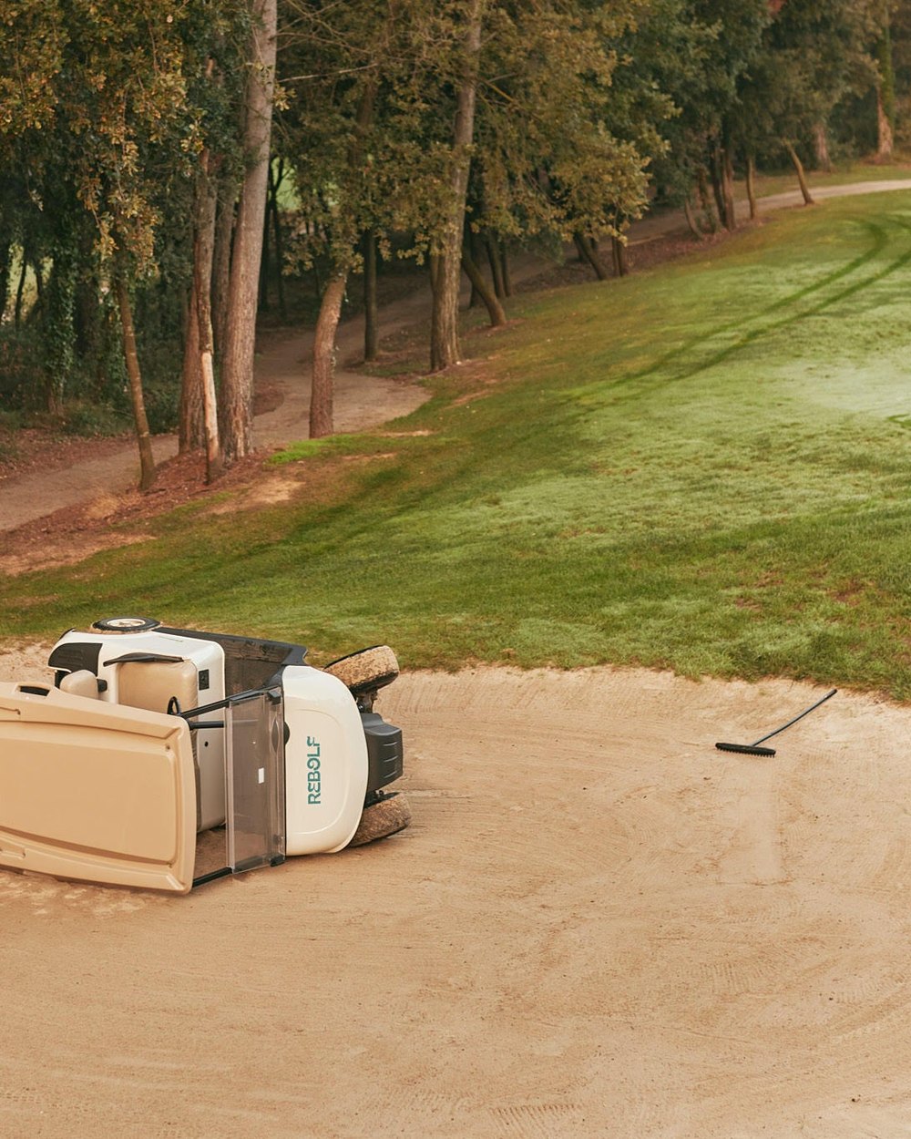 A Rebolf golf buggy tipped over on its side in a sand bunker