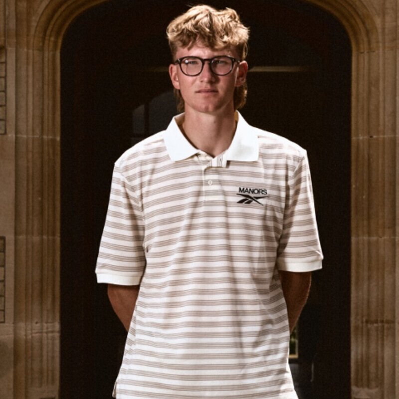 Striped Reebok x Manors polo shot in a stone doorway