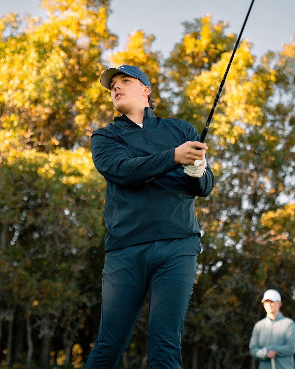 A golfer in a navy quarter zip finishing his swing