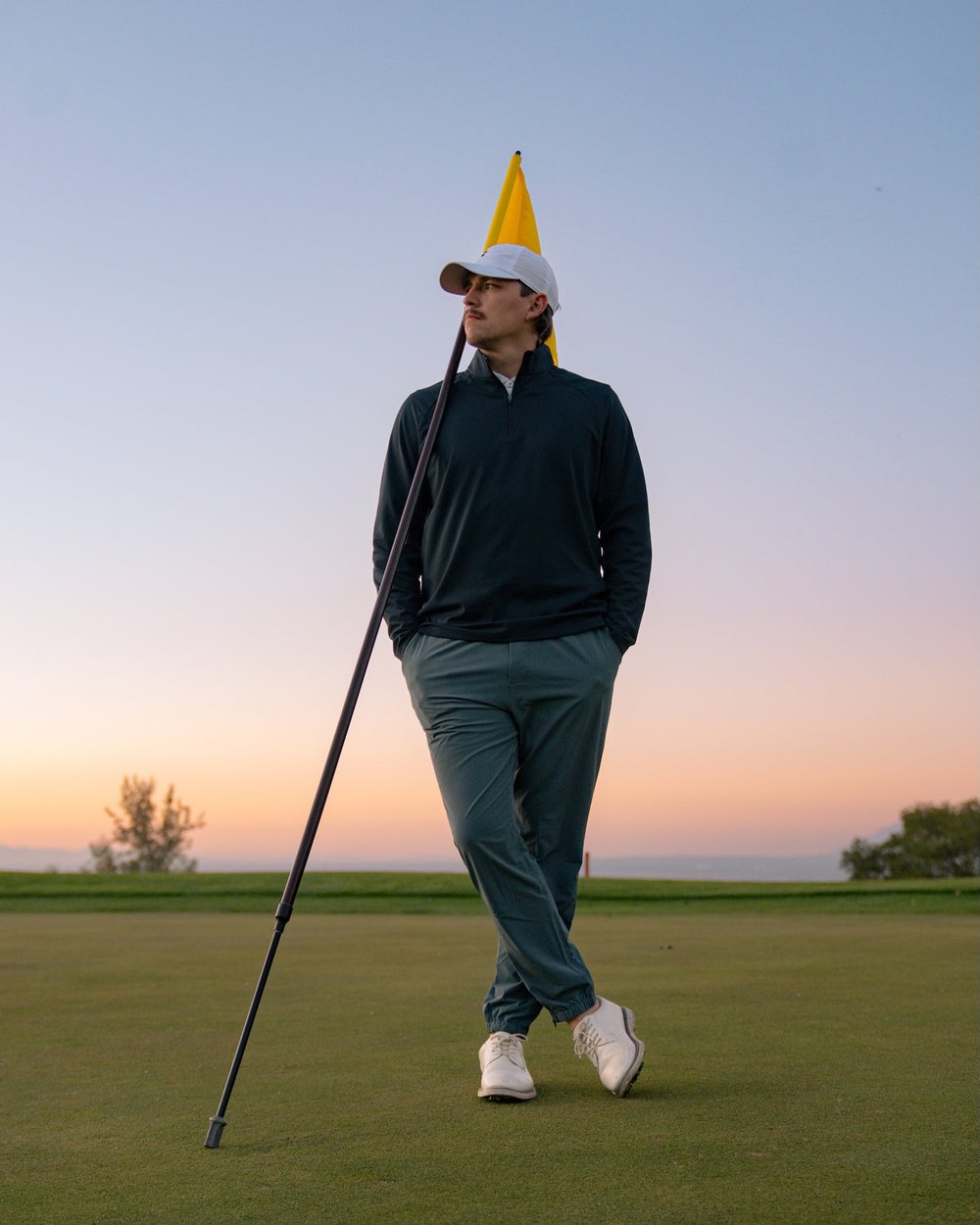 A golfer in a navy top and jogger standing on a green at dusk