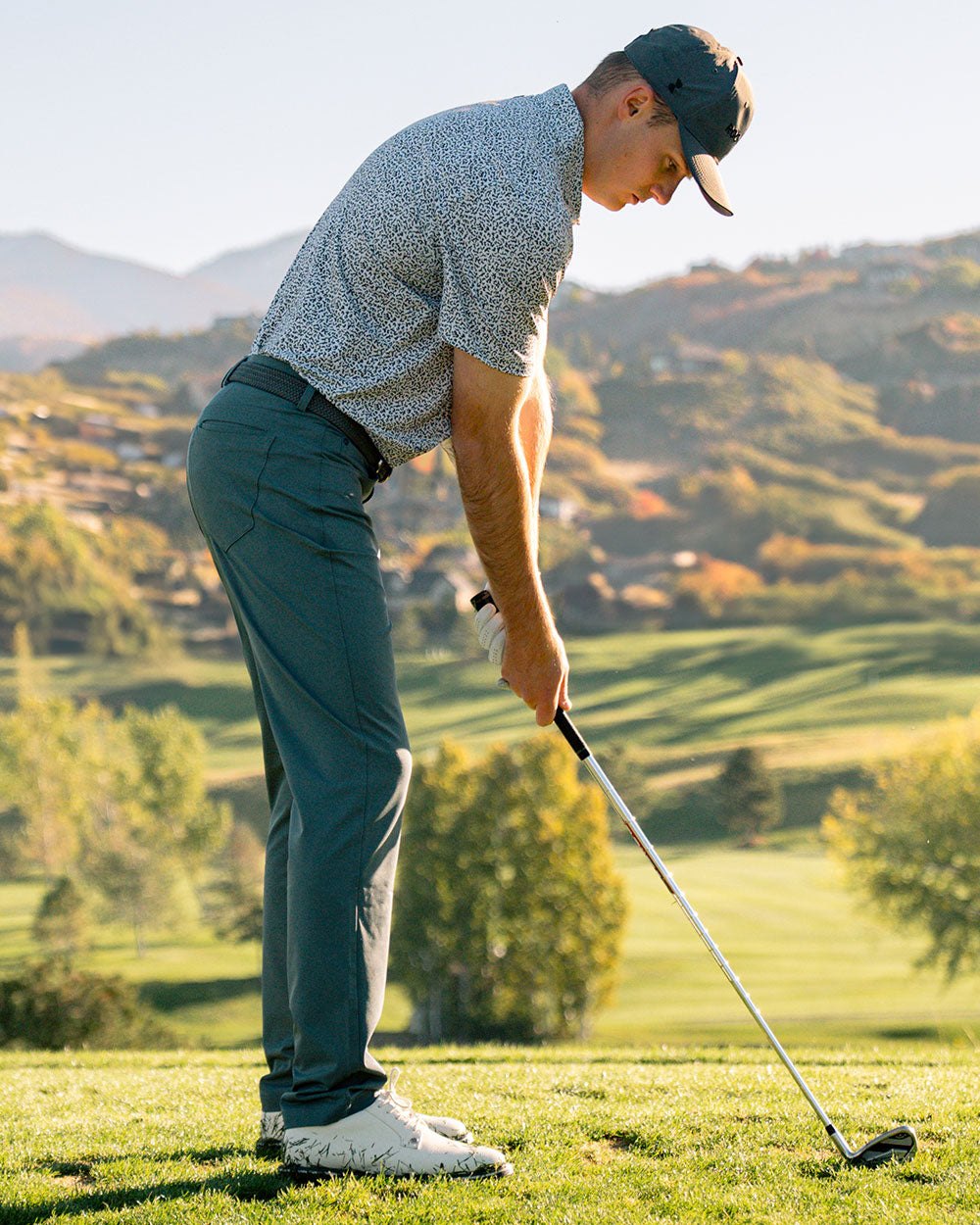 A golfer reading a putt in moss pants on a hillside course