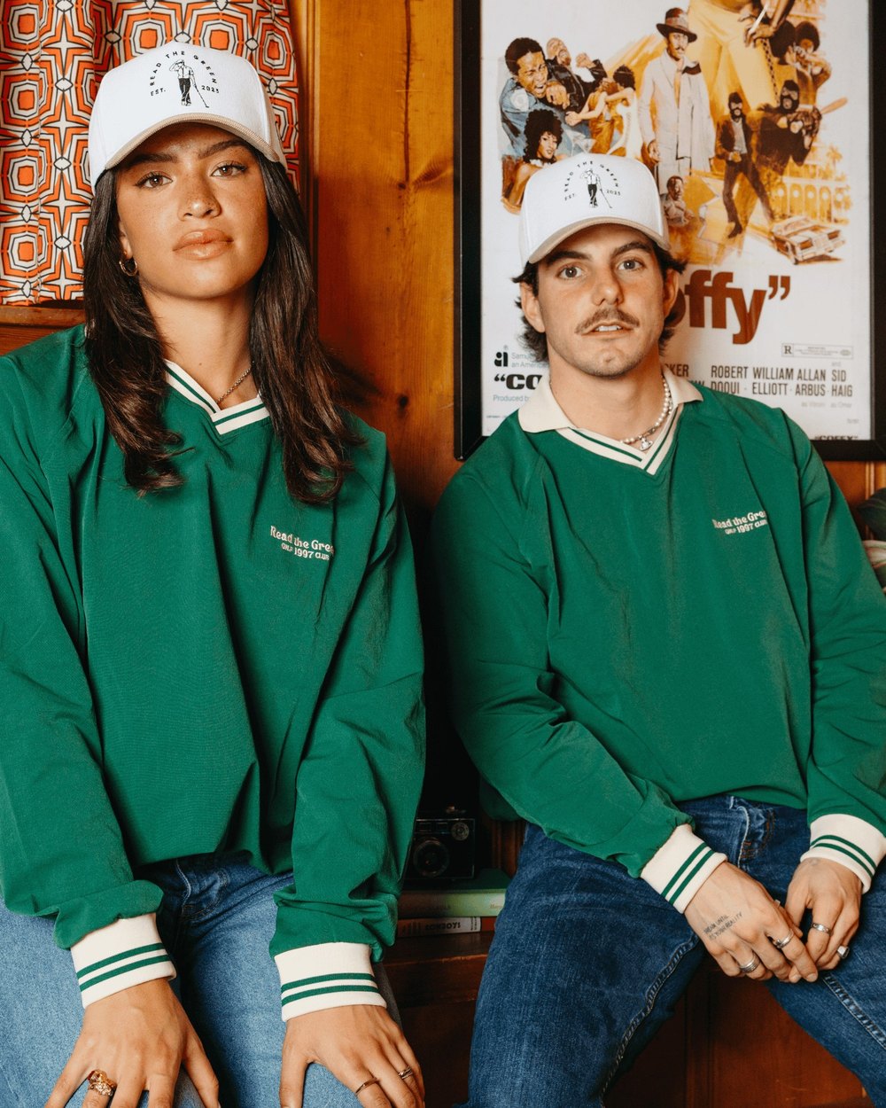 Two models in green &rsquo;97 Vintage Pullovers sitting in a wood-paneled room