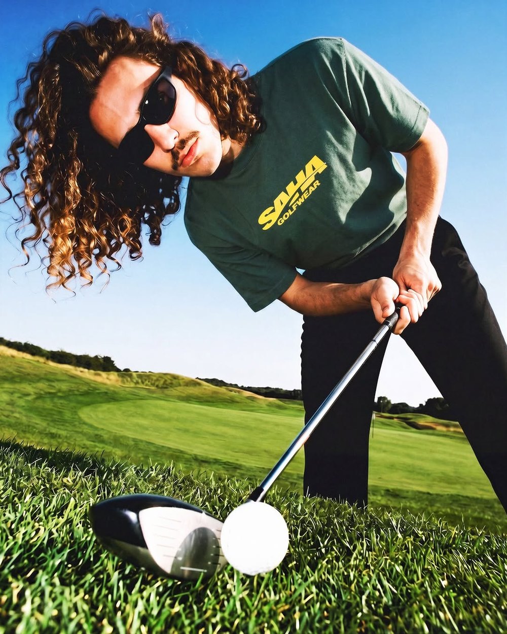 A golfer in sunglasses and the green Slice Tee teeing up a ball