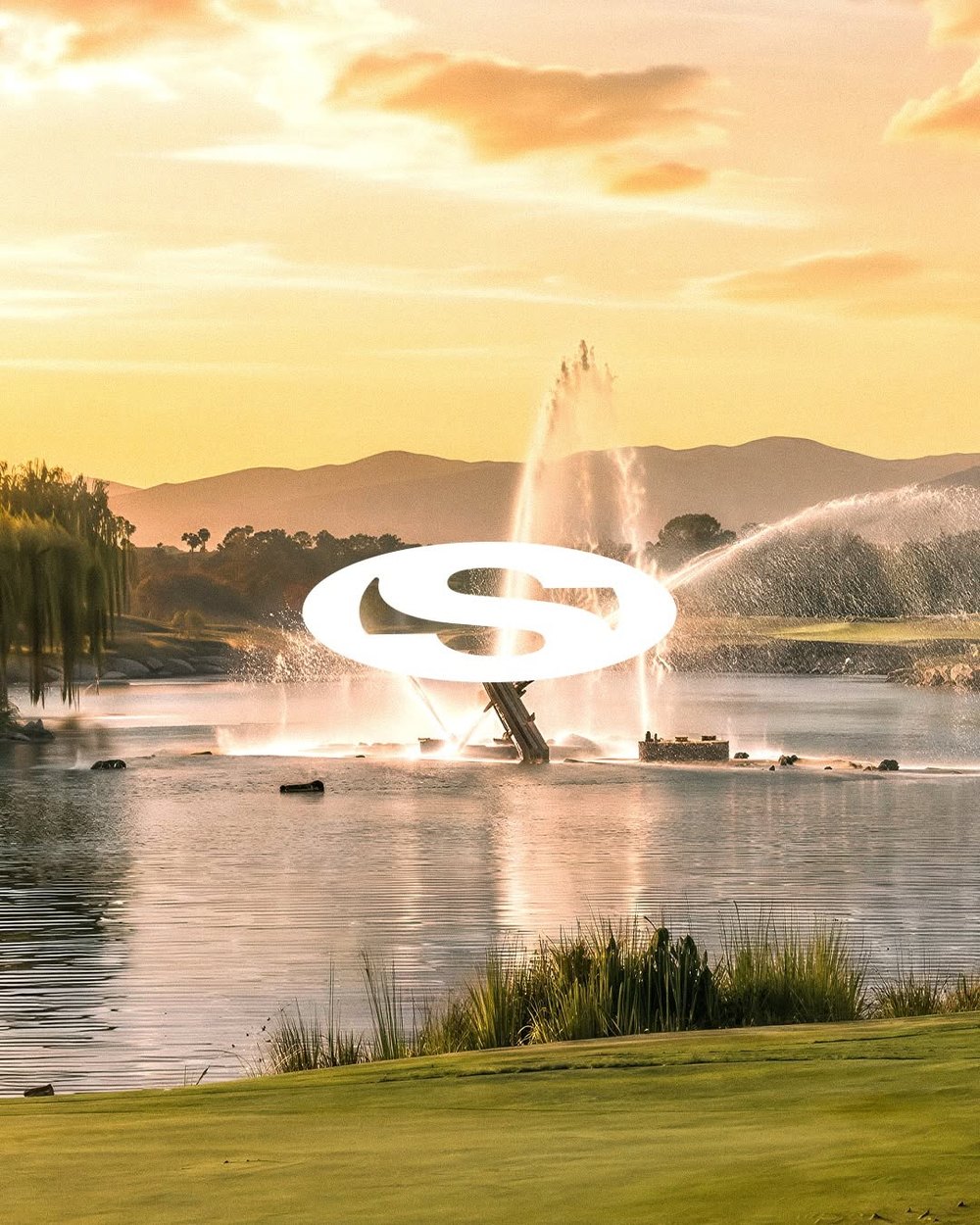 The Saha oval logo over a lake fountain at sunset