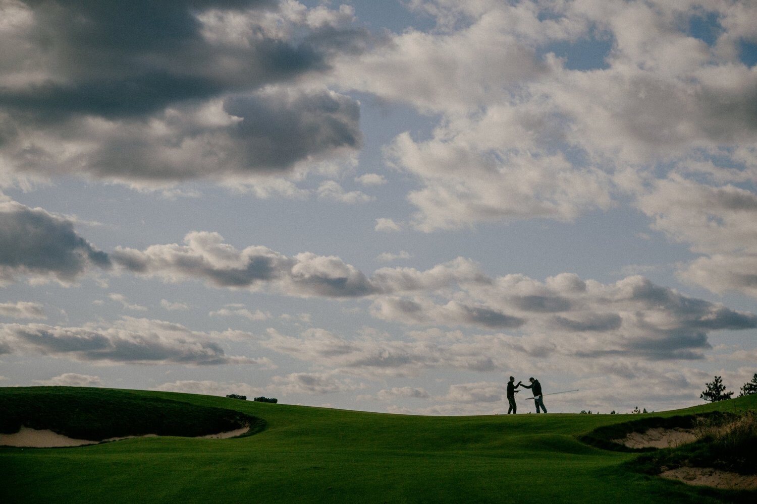 Two golfers on a Sand Valley green under big clouds — Sentinel Basecamp Expedition One