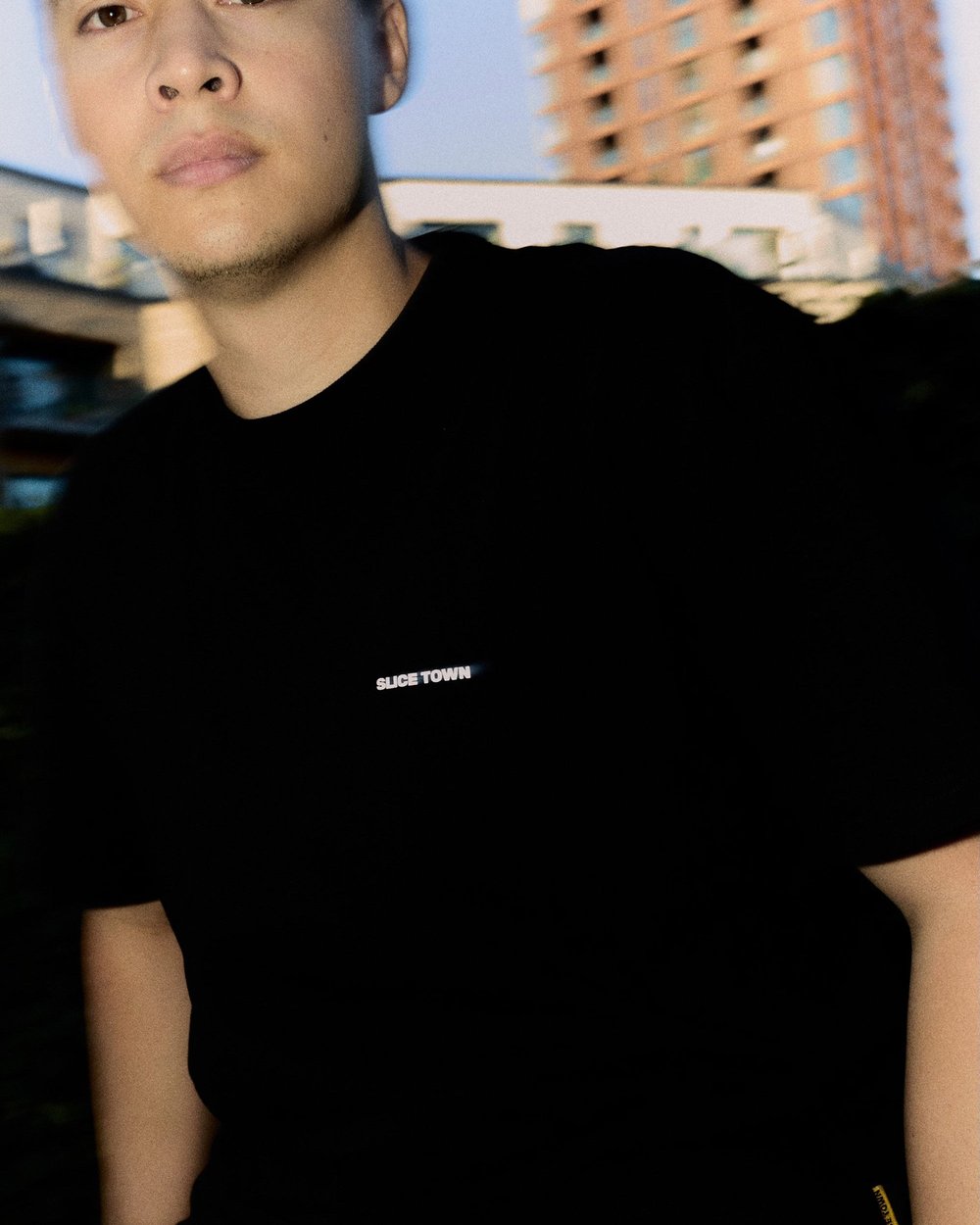 A man in a black SLICE TOWN tee in front of a tower block