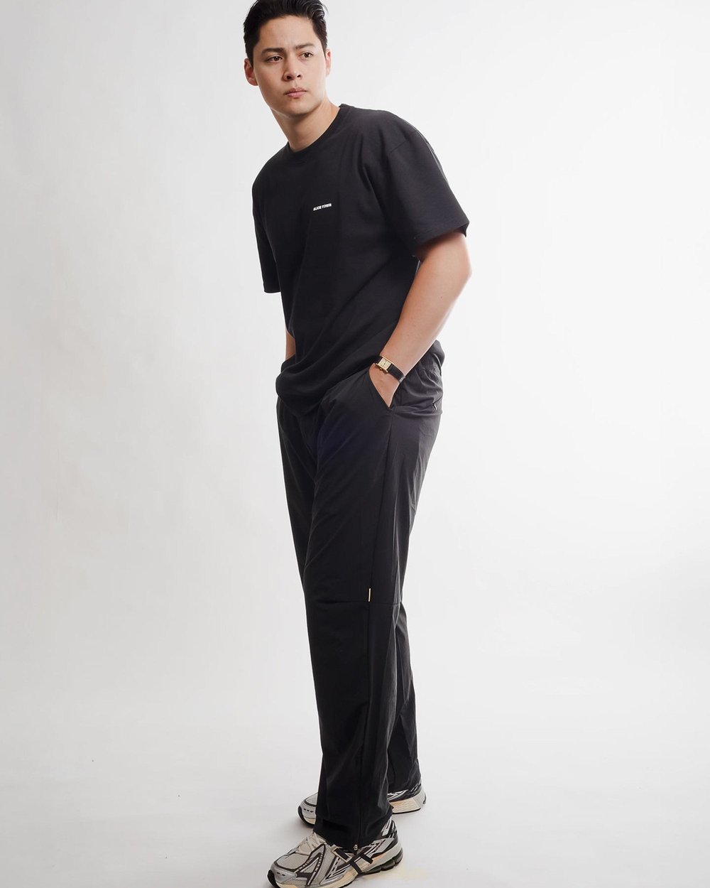 A man in a black tee and black tech pants in a white studio
