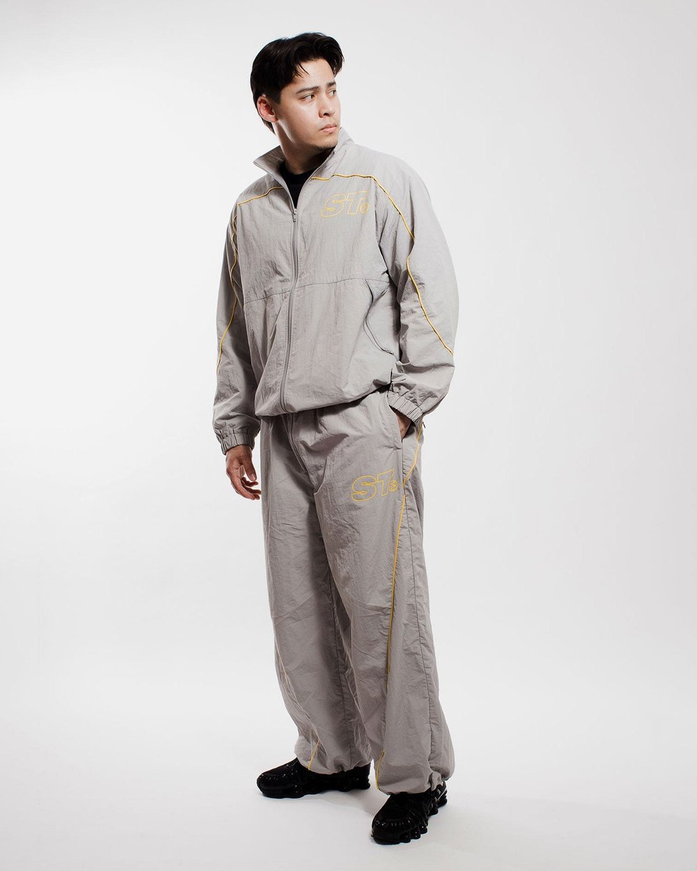 A man in the slate track jacket and pants in a white studio