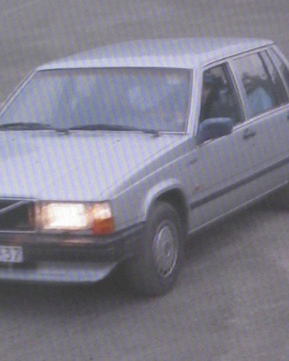An old silver Volvo saloon with its headlights on
