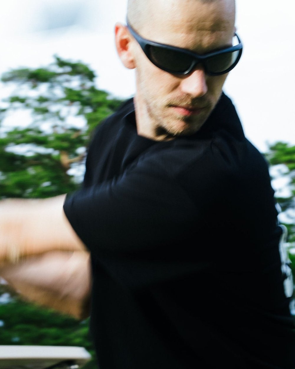 A golfer in wraparound sunglasses and a black tee mid-swing