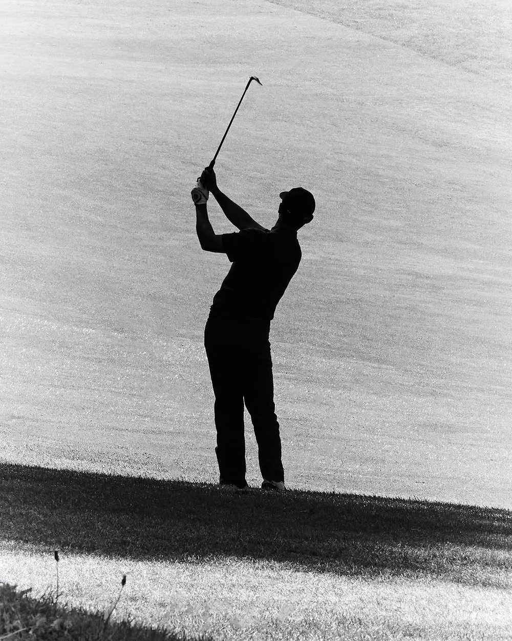 Black-and-white silhouette of a golfer at the finish on a fairway