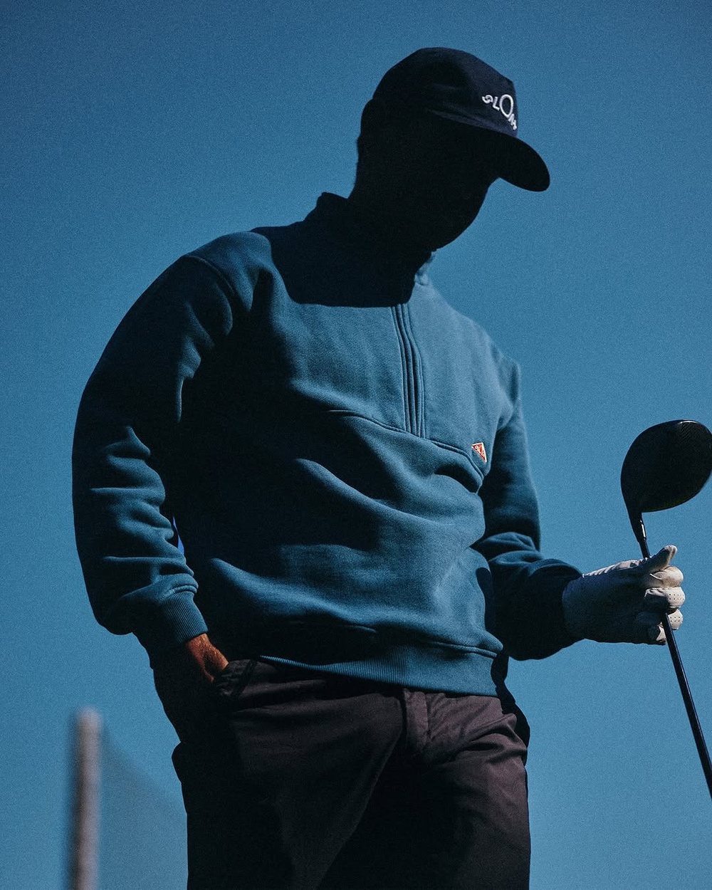 A golfer in a blue fleece quarter zip holding a driver against a blue sky