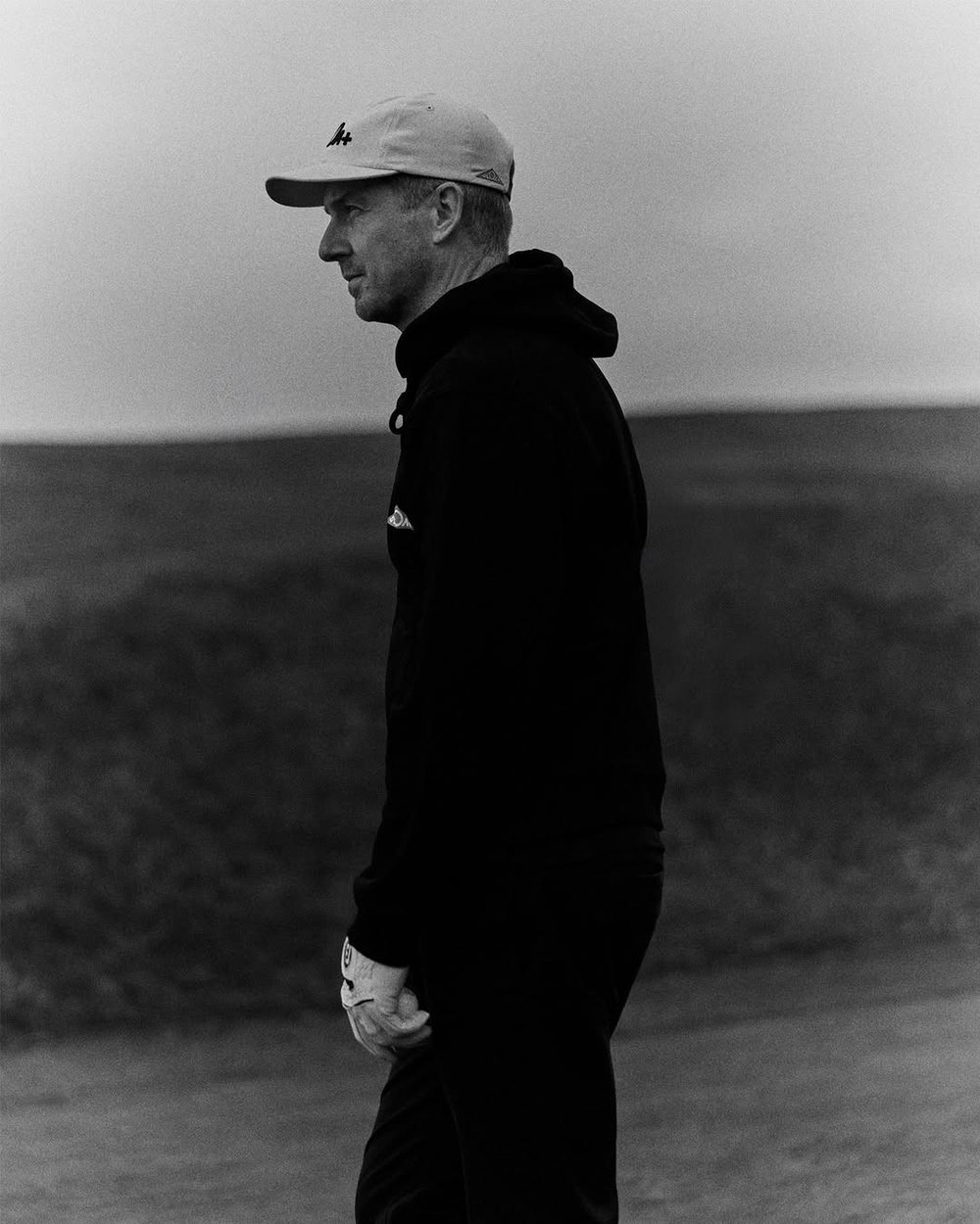 Black-and-white photo of a golfer in a black hoodie on a coastal course