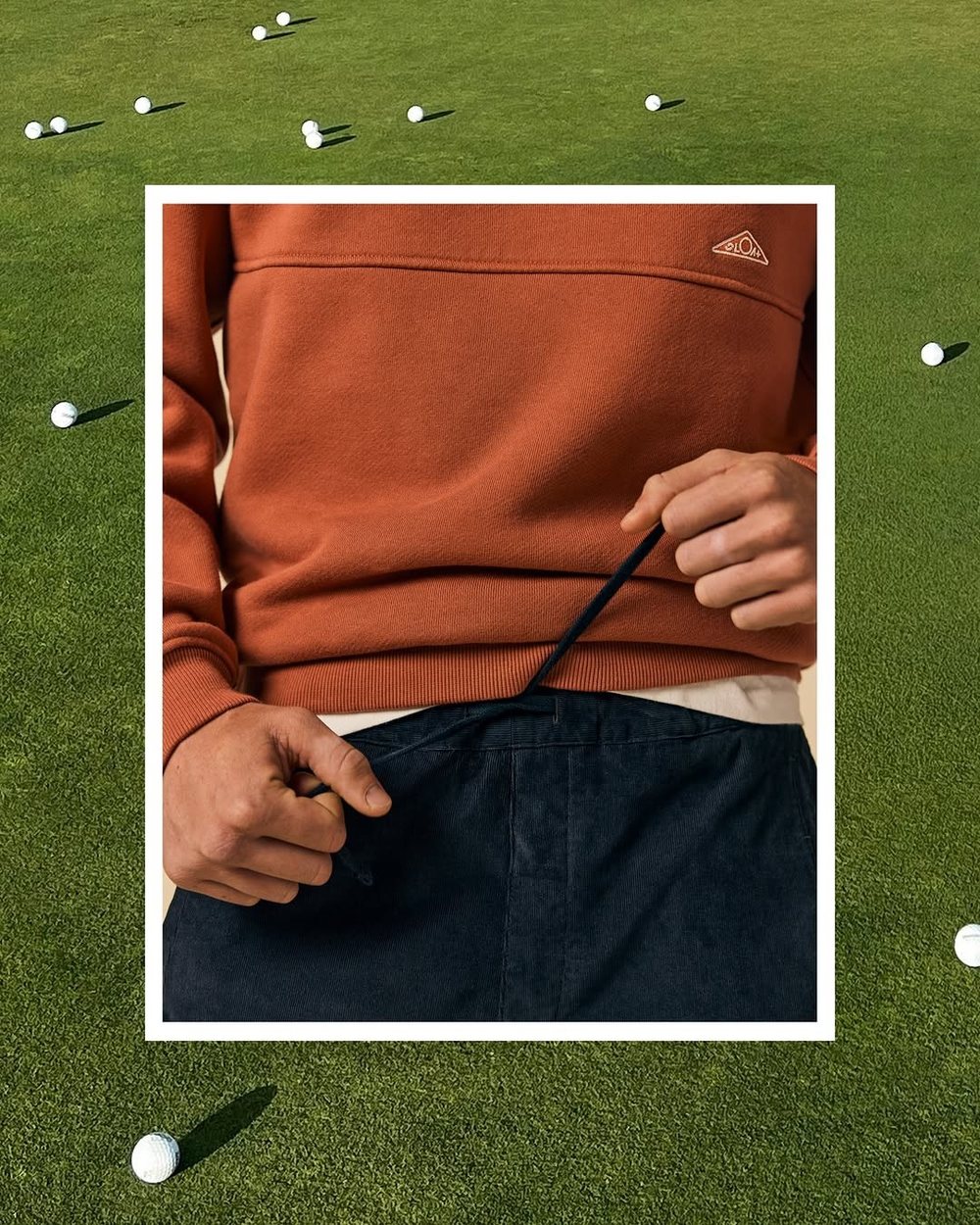 A rust SLOAT crewneck and navy corduroy shorts on a range scattered with balls
