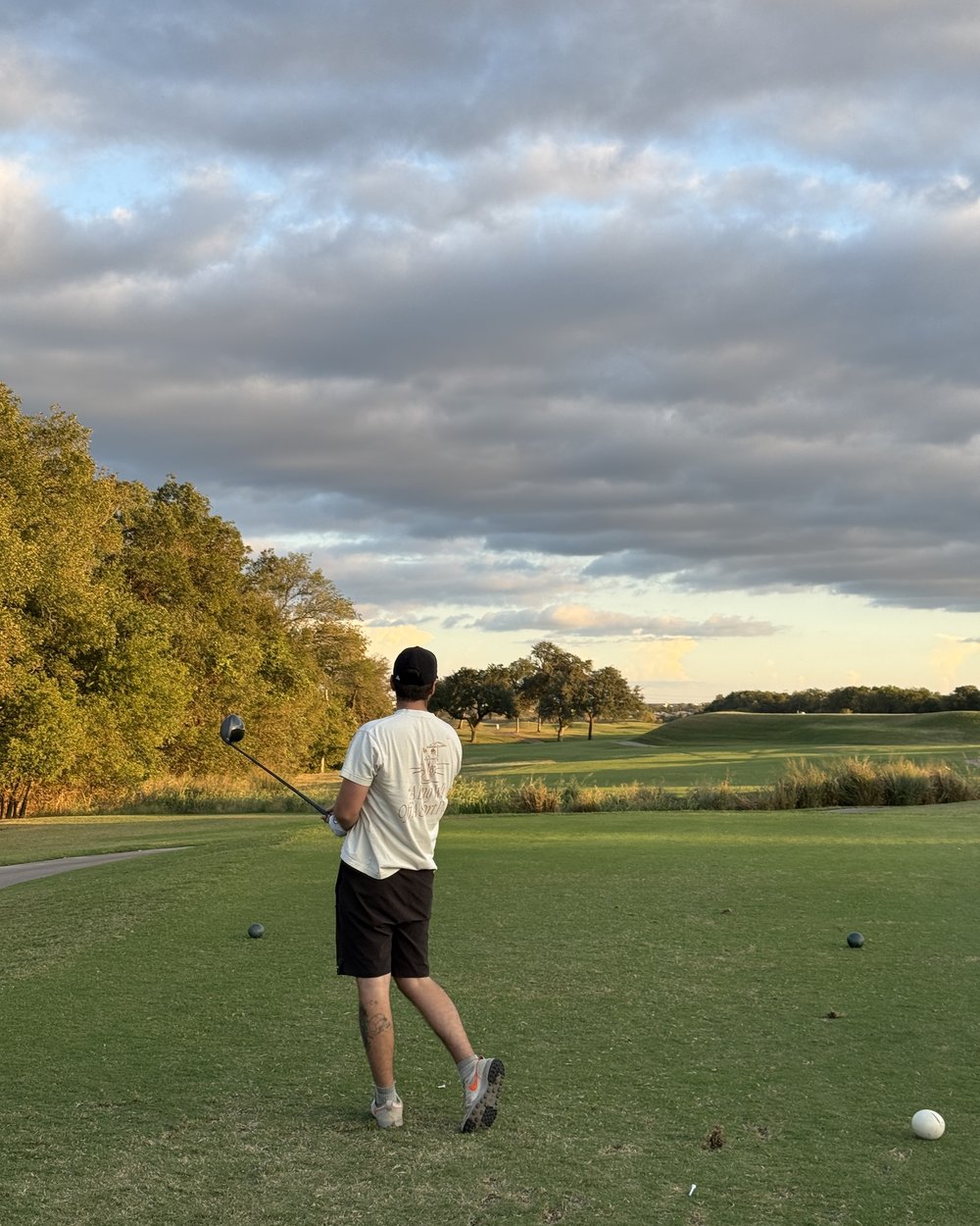 A golfer watching his tee shot under a layered evening sky at Jimmy Clay