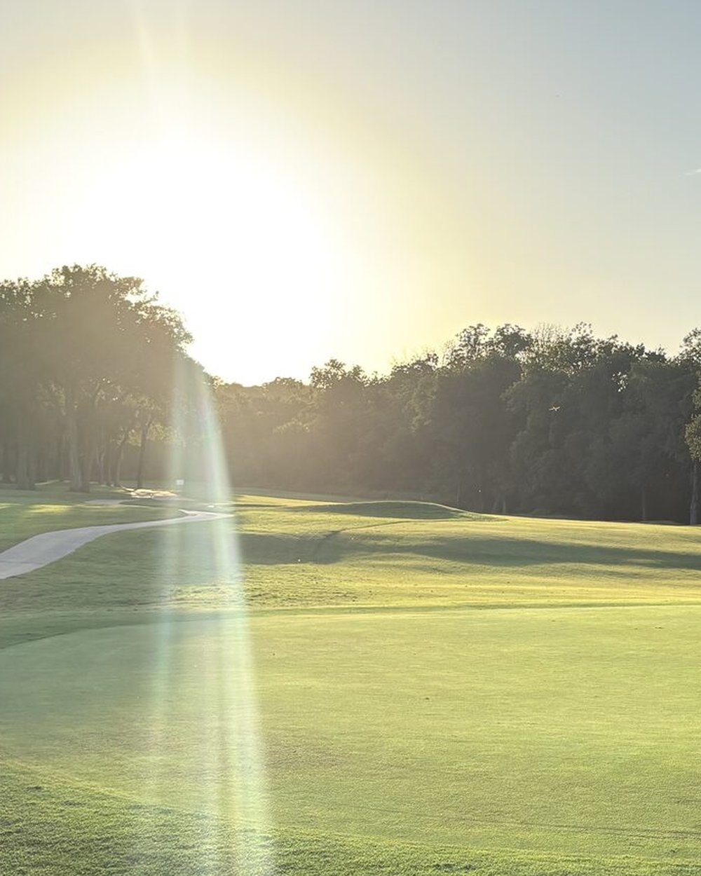 The low sun flaring over a green and flag at Jimmy Clay