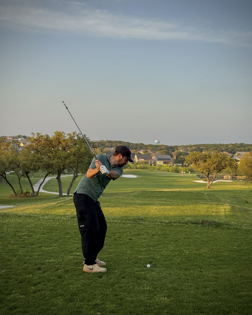 A golfer mid-swing on an evening fairway